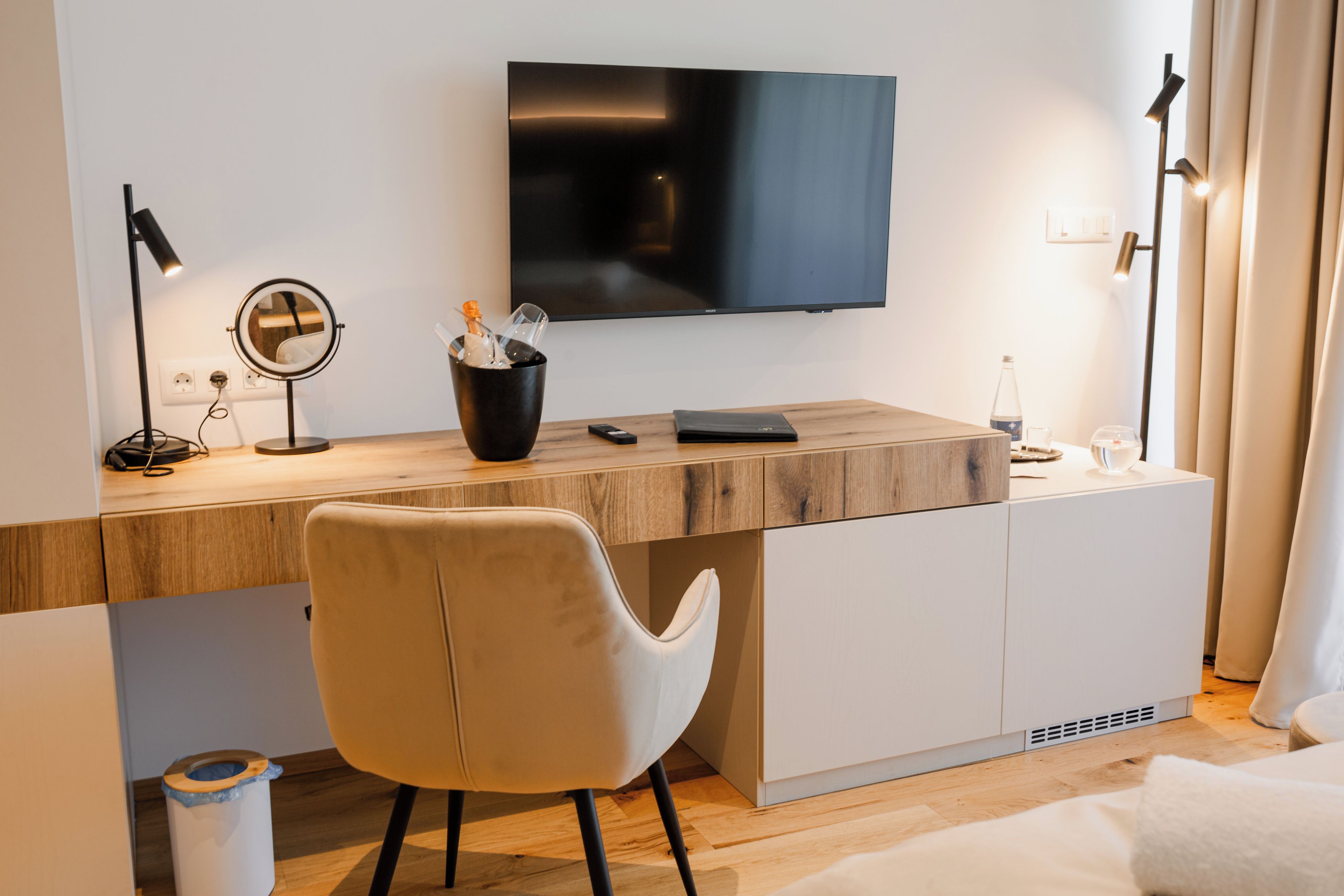 A modern hotel room with a wooden desk, a flat-screen TV, a chair, and a bed.