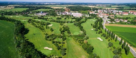 An aerial view of a golf course with sand bunkers, a large building complex, and surrounding residential areas.