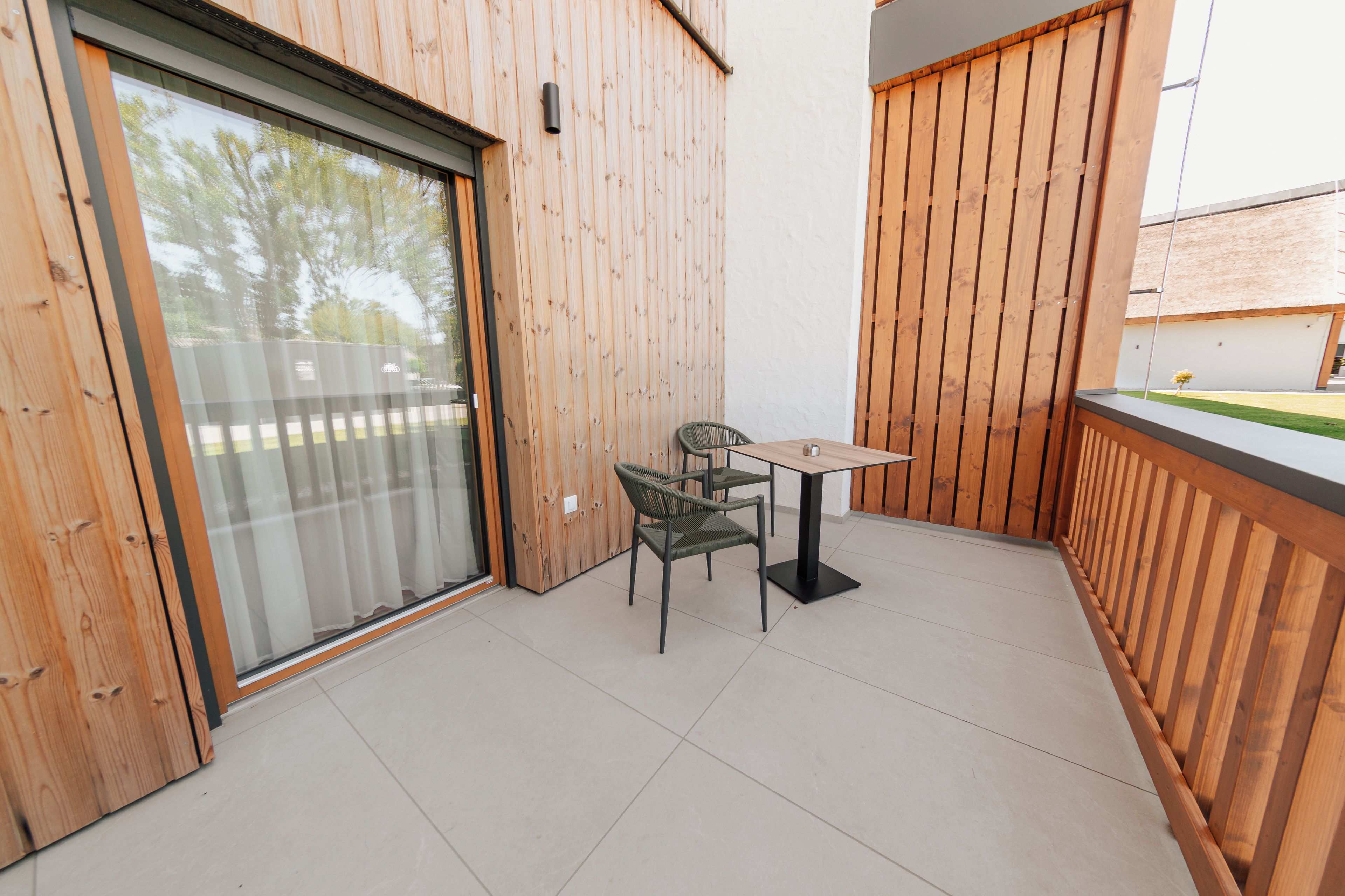 A balcony with a table and chairs, wooden walls, and a sliding glass door.