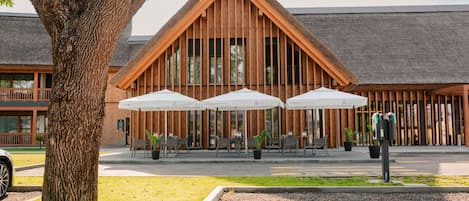 Un edificio con techo inclinado, fachada de madera y zona de estar exterior con sombrillas.