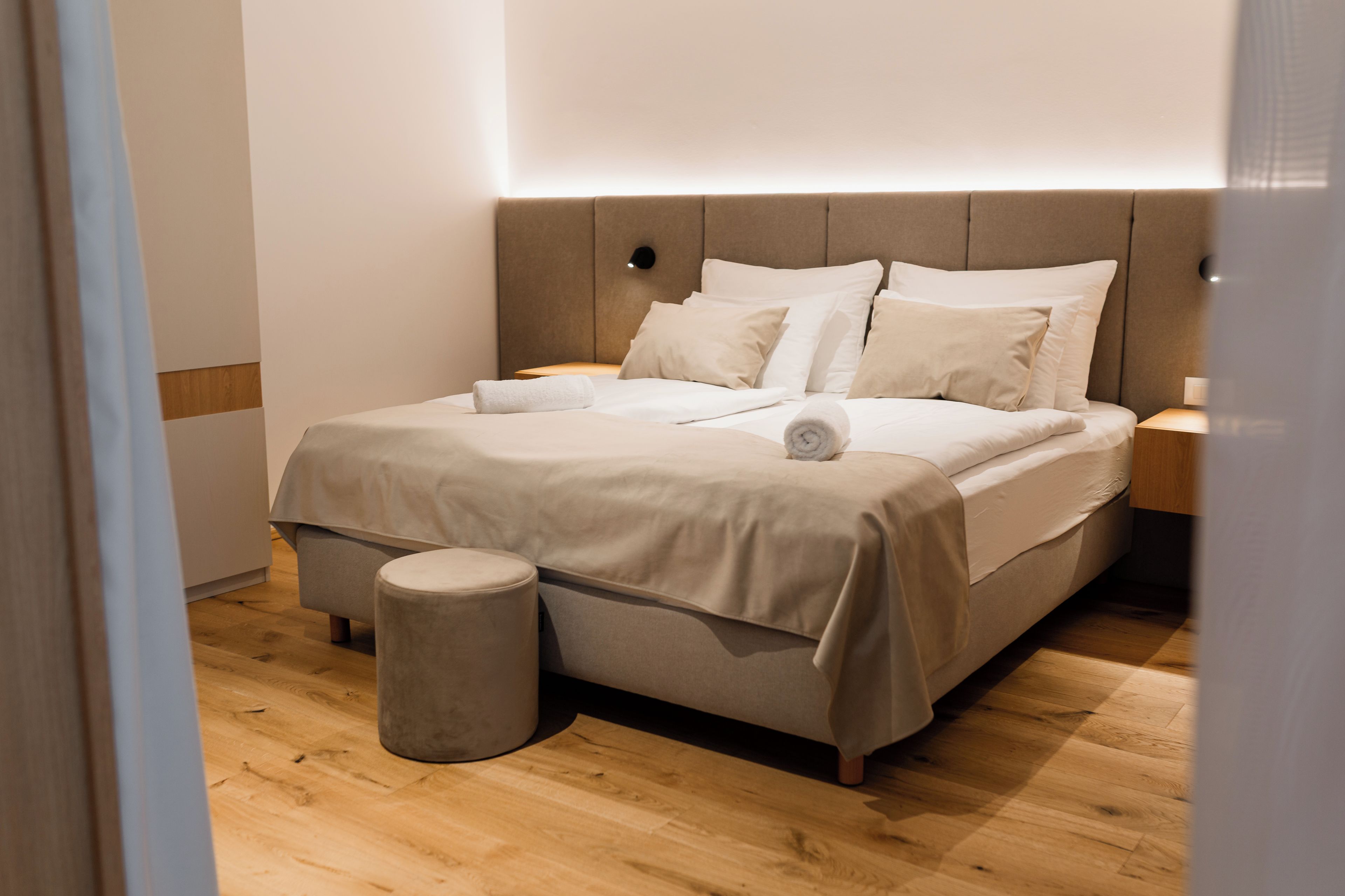 A modern bedroom with a bed, bedside tables, and a small stool.