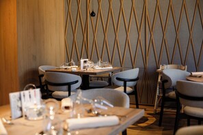 A restaurant interior with a wooden wall, a geometric patterned wall, and a table set with glasses and cutlery. - Boutique Hotel Sončno Polje (Moravske Toplice)