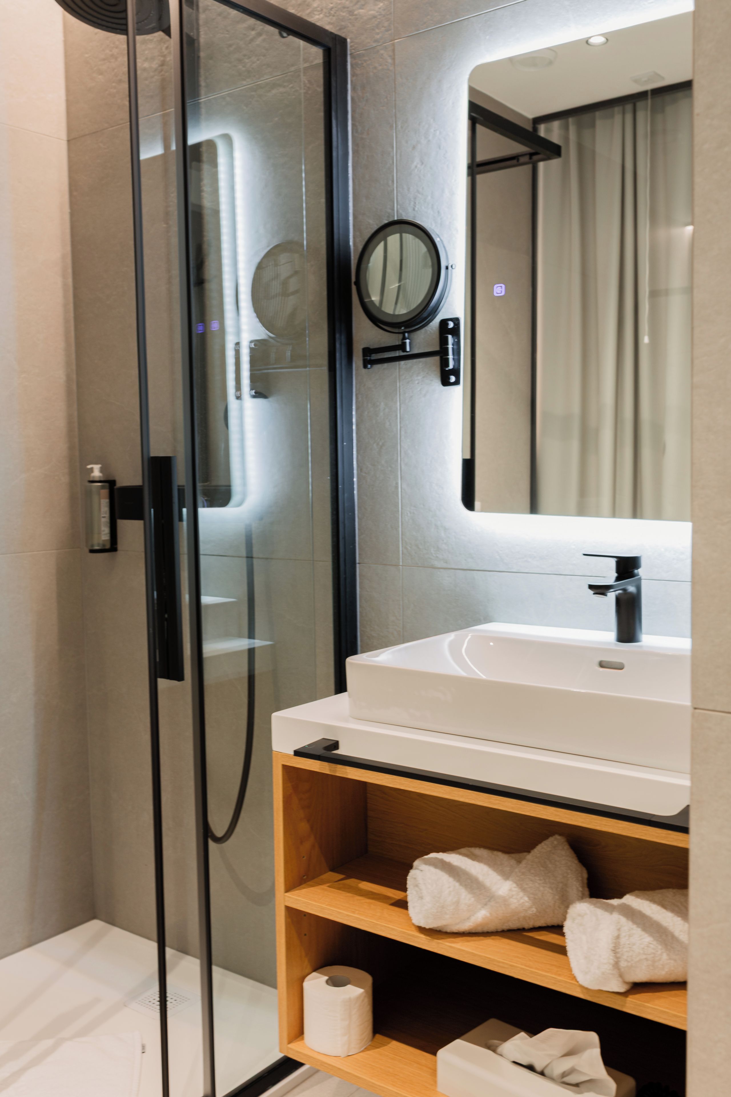 Une salle de bain moderne avec une douche à l’italienne en verre, un lavabo blanc avec un robinet noir et un miroir au-dessus du lavabo.