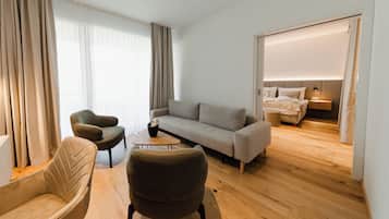 A modern hotel room with a sofa, armchairs, a small table, and a bed with a nightstand.