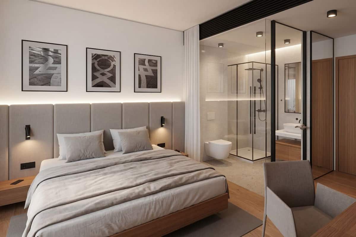 A modern bedroom with a large bed, bedside tables, a chair, a glass-enclosed shower, and a wooden wardrobe.