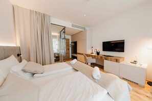 A hotel room with two beds, a desk, a television, and a bathroom visible through a glass partition. - Boutique Hotel Sončno Polje (Moravske Toplice)