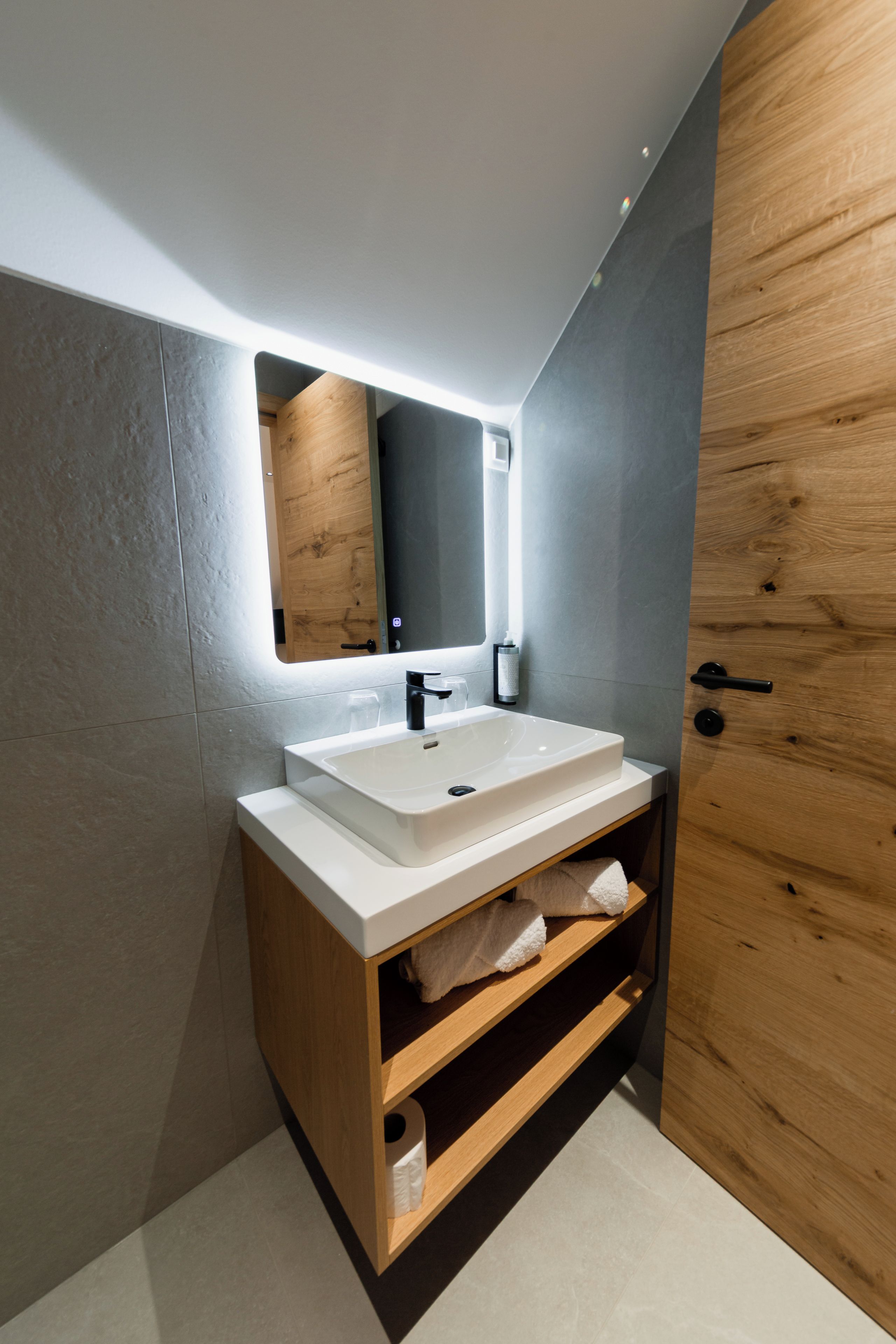 A modern bathroom with a white sink, a mirror, and a wooden door.