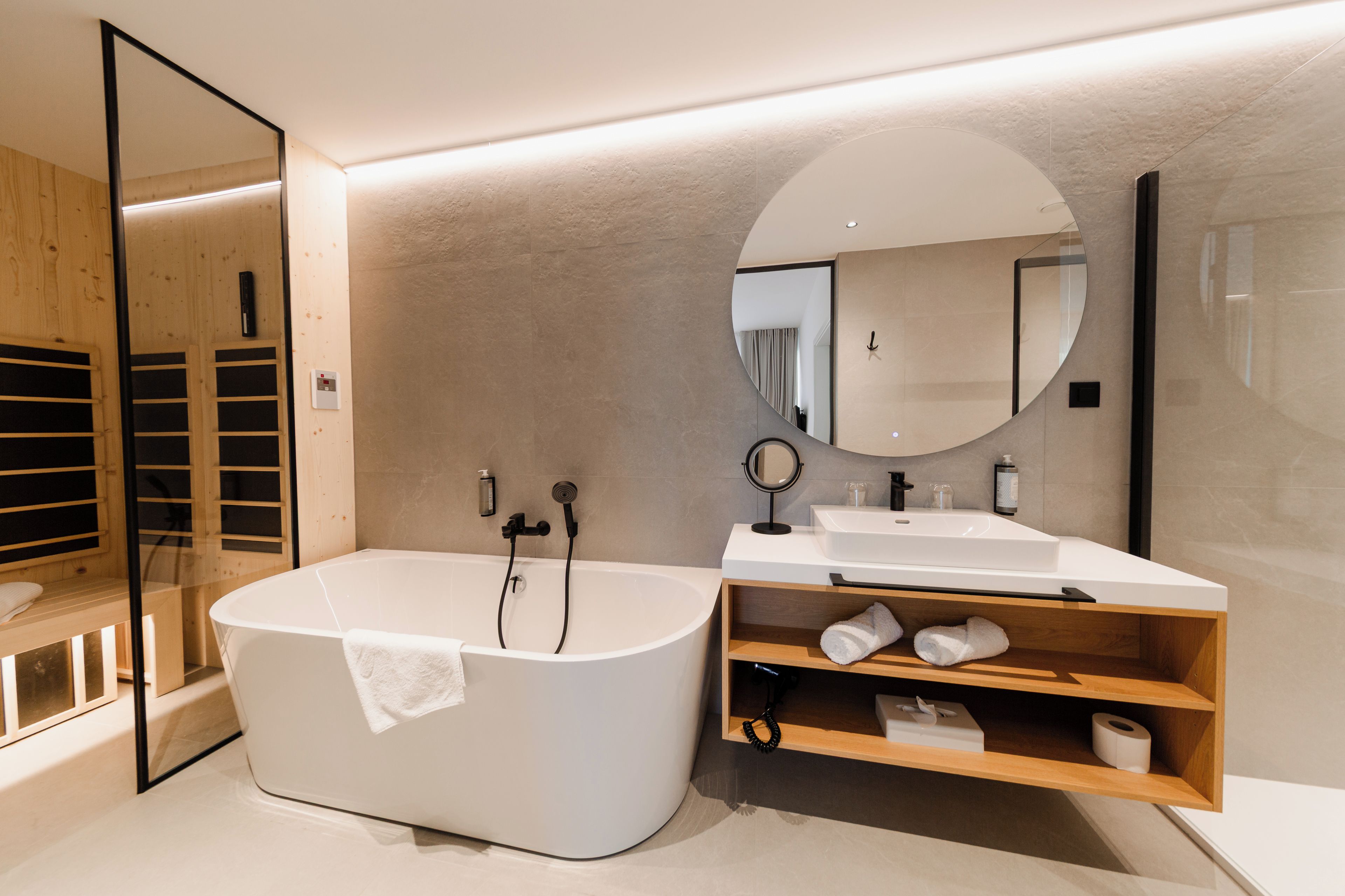 A modern bathroom with a freestanding bathtub, a vanity with a mirror, and a wooden shelf.