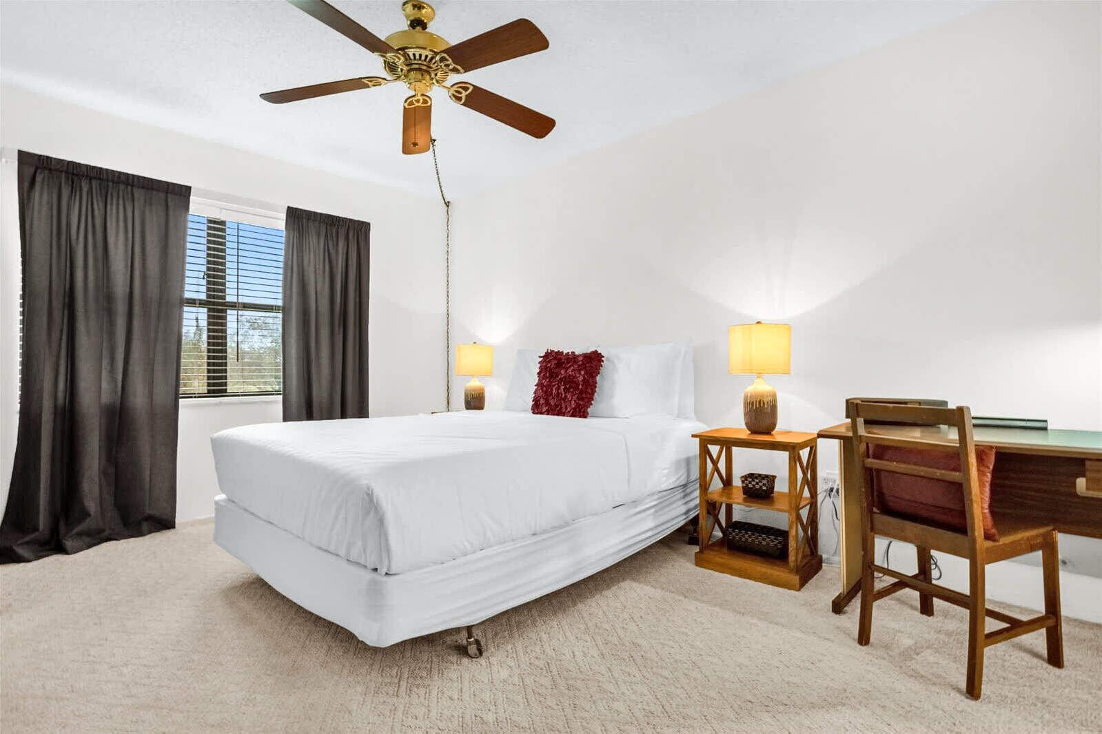 Habitación de hotel con cama, escritorio, silla, ventilador de techo y dos lámparas de noche.