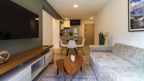 Una sala de estar moderna con un televisor de pantalla plana, una mesa de centro de madera, un sofá gris y un comedor con mesa y sillas.