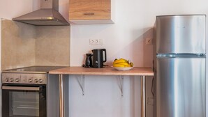 Et køkken med en stålfarvet ovn, kaffemaskine, en skål med frugt og et køleskab.