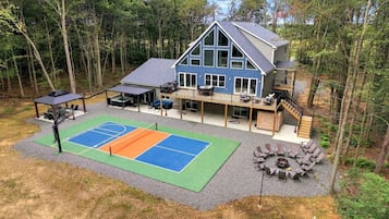 A two-story house with a tennis court, outdoor seating, and a fire pit.