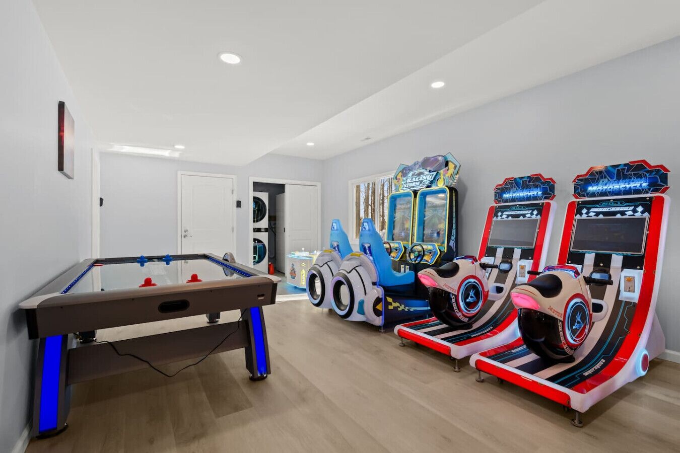 A room with a foosball table, two racing arcade machines, and a pool table.