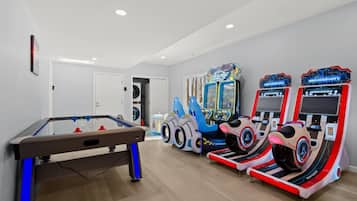 A room with a foosball table, two racing arcade machines, and a pool table.