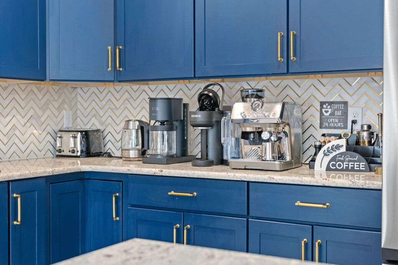 A kitchen with blue cabinets, a coffee machine, a toaster, and a coffee bar sign.