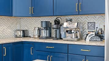 A kitchen with blue cabinets, a coffee machine, a toaster, and a coffee bar sign.
