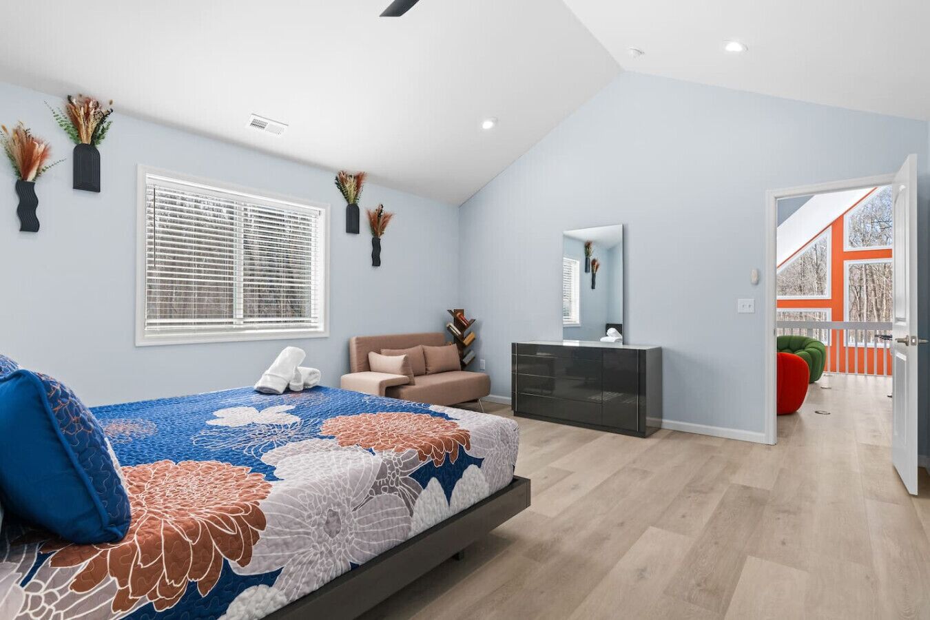 A modern bedroom with a bed, bedside table, dresser, and a window with blinds.