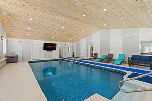 Ein Hallenbad mit Holzbalkendecke, einem Fernsehbildschirm und Liegestühlen.