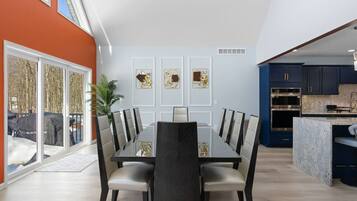A modern dining area with a glass table and chairs, a kitchen with dark cabinets, and a view of the outdoors.