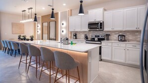 Uma cozinha moderna com ilha central, banquetas, iluminação pendente e armários brancos.