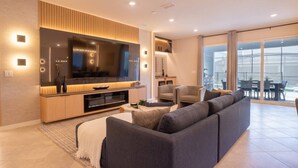 Uma sala de estar moderna com uma grande TV de tela plana, um sofá e uma área de jantar com mesa e cadeiras.