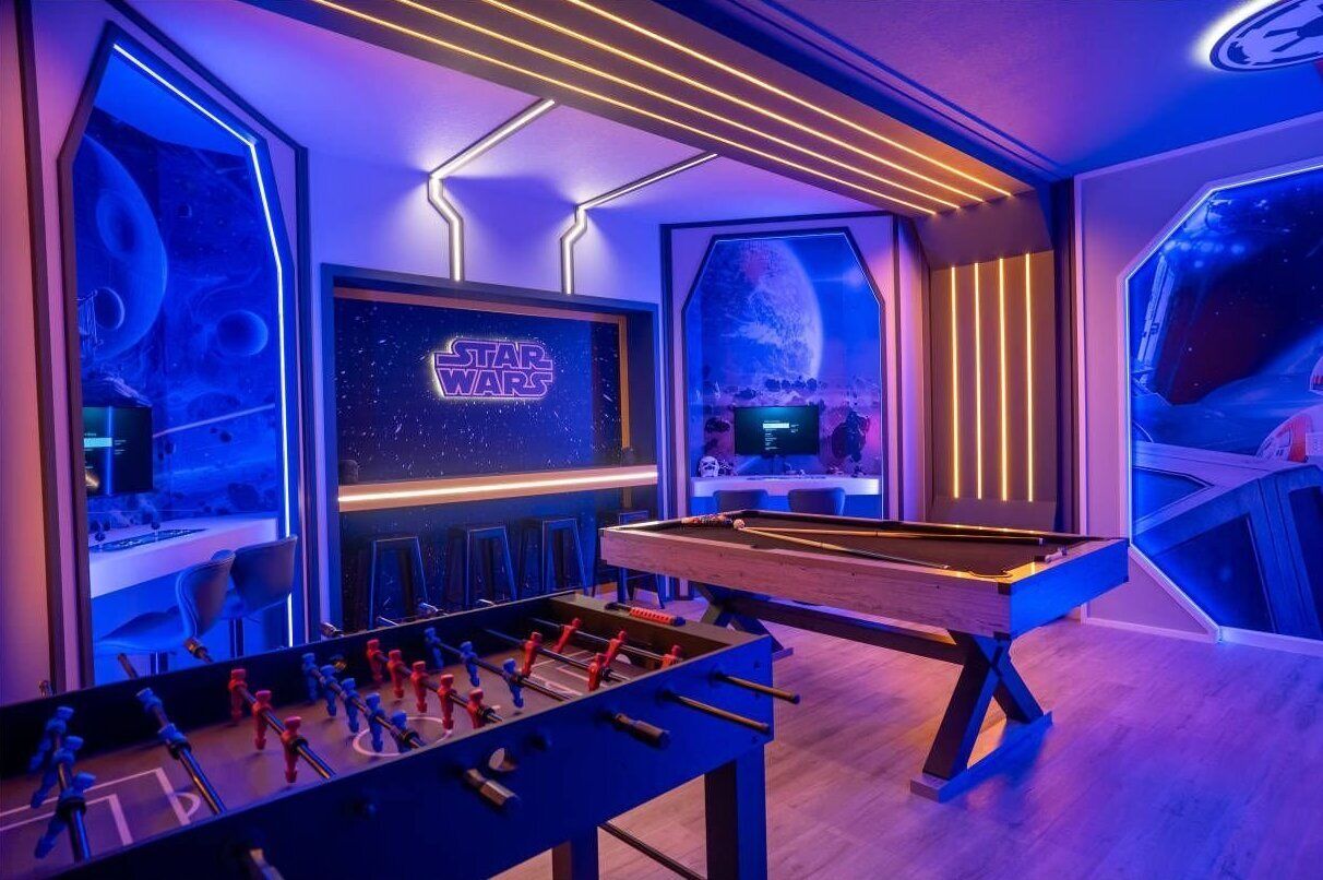 Ein Raum mit Billardtisch, Kicker und Star Wars-Dekor, einschließlich Wandbildern und Neonlichtern.