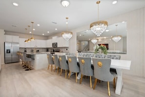 A modern kitchen with a central island, bar seating, and a dining area with a large mirror and chandelier. - 10BR Villa w/ Star Wars Theater & Game Room (Davenport)