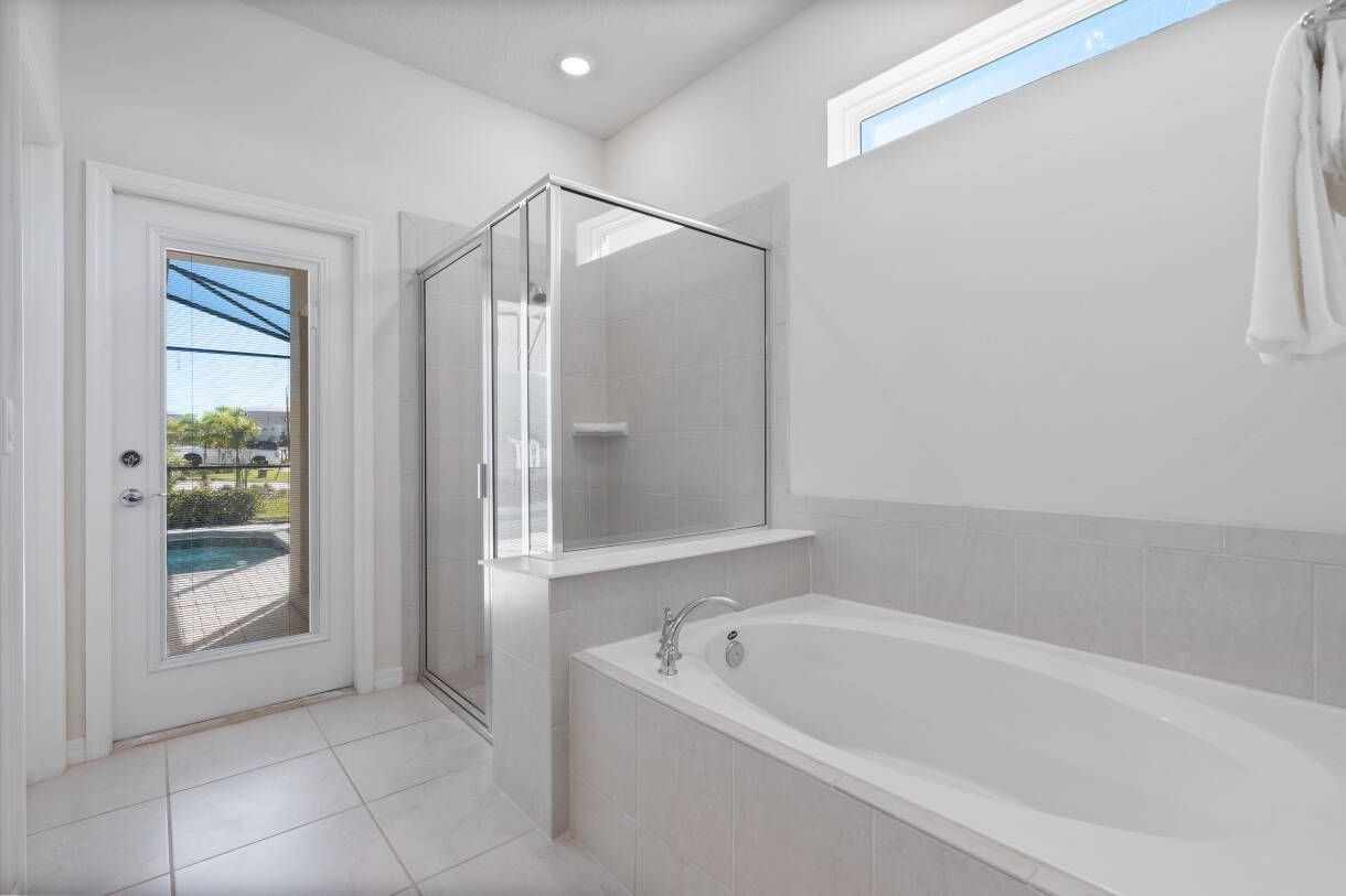 Un baño moderno con ducha envuelta en vidrio, una bañera grande y una puerta que da a una piscina.