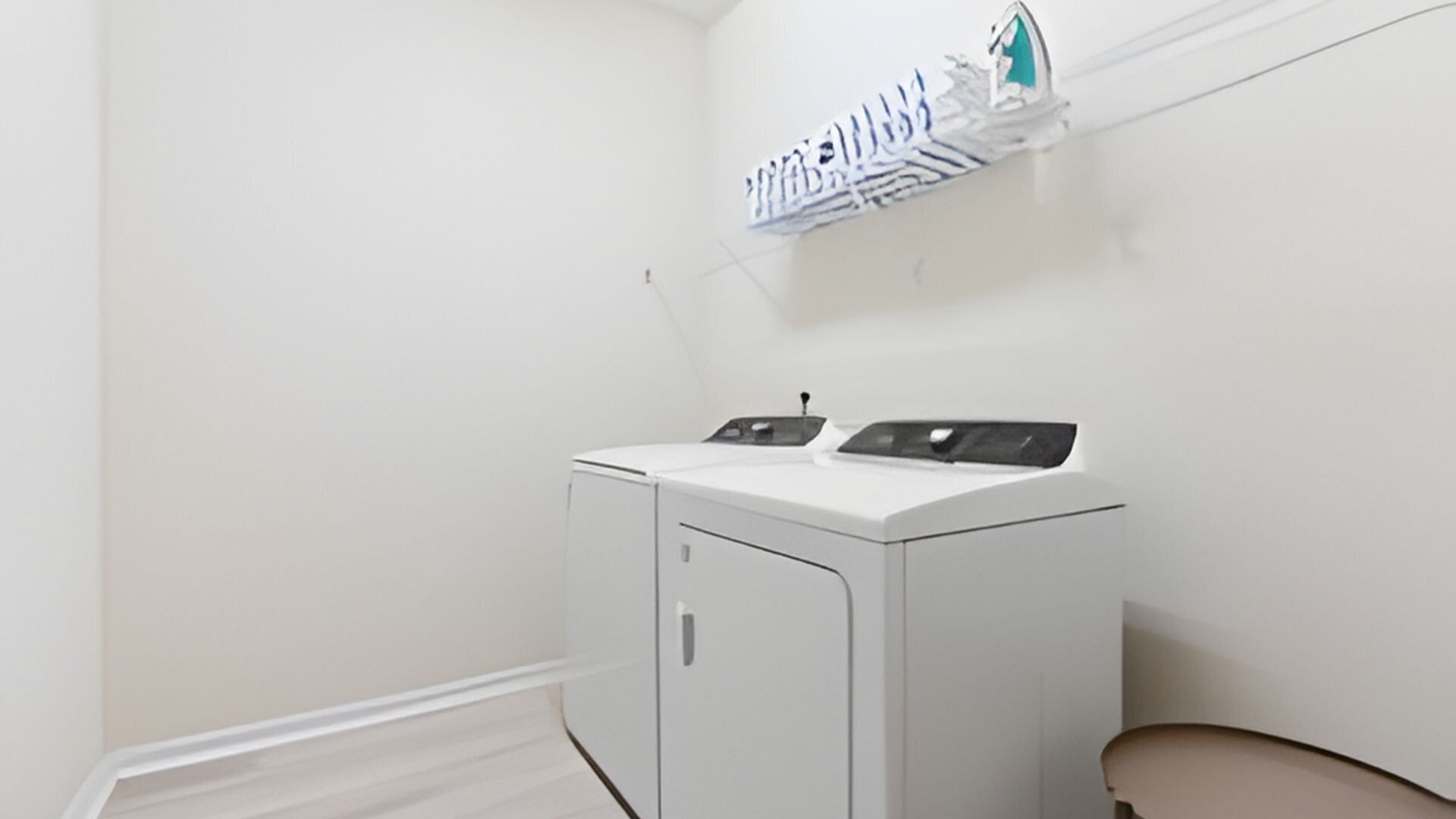 A compact laundry room with a front-loading washer and dryer, a small shelf with folded clothes, and a plain white wall.