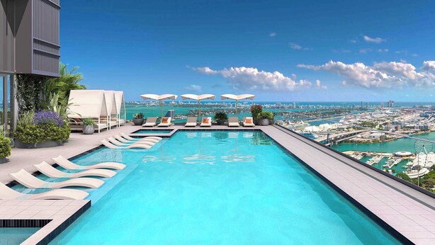 Una piscina infinita en la azotea con sillones y sombrillas, con vistas a un paisaje urbano y al agua.