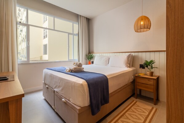 Een slaapkamer met een groot bed, een nachtkastje, een raam en een hanglamp.