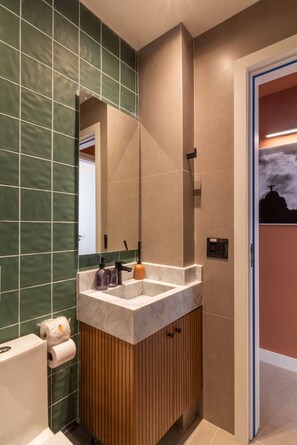 Un baño moderno con un espejo grande, azulejos verdes, un mueble de tocador de madera y un inodoro.