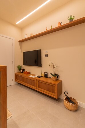 Een moderne receptie met een houten console tafel, een flatscreen televisie aan de muur en een klein plankje met decoratieve objecten.