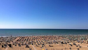 Una playa con hileras de sombrillas y tumbonas, una torre de socorristas y el océano al fondo.