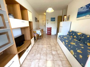 Ein gemütlicher, kompakter Wohnbereich mit Sofa, Fernseher, Holzregalen, Esstisch und Küchenzeile.
