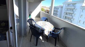 Un balcón con mesa y sillas, vistas a edificios y un toldo a rayas verdes.