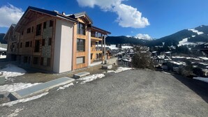 Un edificio de madera de varios pisos con balcones, frente a un paisaje de montañas nevadas y un cielo azul despejado.
