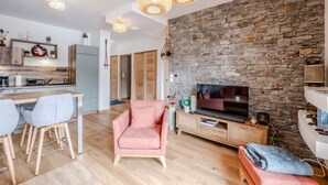 Una sala de estar moderna con una pared de piedra, un televisor y un comedor con sillas.