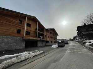 Un immeuble en bois à plusieurs étages, avec une base en pierre, un espace de stationnement enneigé et un ciel dégagé.