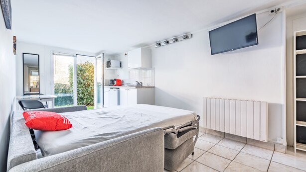 Ein modernes Schlafzimmer mit Bett, Fernseher, Heizkörper und Blick ins Freie.