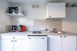 A modern kitchen with white cabinets, a built-in microwave, a coffee maker, a kettle, and a sink. - Adour Océan Lodge - Proche Plage (Anglet)