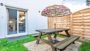 Ein Holztisch für ein Picknick mit einem bunten Sonnenschirm, ein Holzzaun und ein weißes Gebäude mit Glastür.
