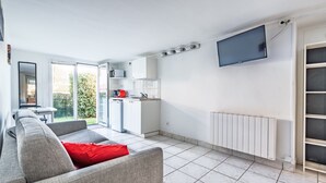 Ein modernes Wohnzimmer mit einem grauen Sofa, einem roten Kissen und einer Küchenzeile, an der ein Fernseher hängt.