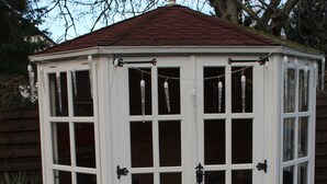 Un abri de jardin en bois, de couleur blanche, doté de nombreuses fenêtres et d’un toit rouge.