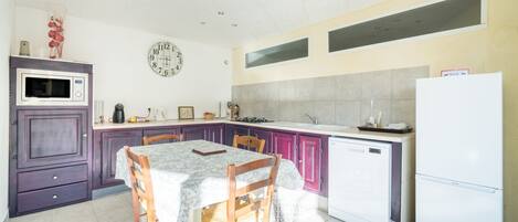 A kitchen with a dining table, chairs, a microwave, a refrigerator, and a clock on the wall.