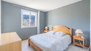 Ein Schlafzimmer mit einem hölzernen Bett, zwei Nachttischen mit Lampen, einem Fenster mit Blick auf eine Landschaft und einer Holzkommode.