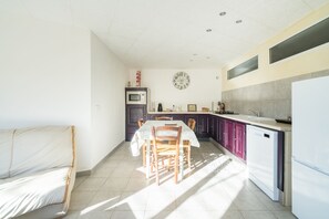 A kitchen with a dining table, chairs, a microwave, a refrigerator, and a clock on the wall. - La Parenthèse de l'Ibie - Proche des Monts d'Ardèche (Villeneuve-de-Berg)