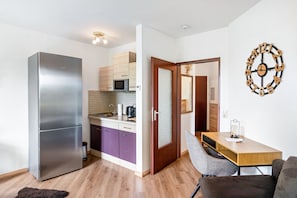 A compact kitchen with a refrigerator, microwave, and purple cabinets, leading to a dining area with a wooden table and chairs.