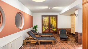 Et sparum med træliggestole, en radiator, en plante og udsigt til en skov gennem en glasdør.