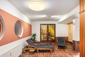 A spa room with wooden loungers, a radiator, a plant, and a view of a forest through a glass door.